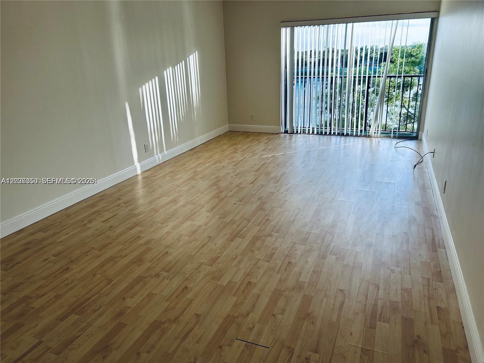 An empty room features light wood-look flooring, beige walls, and a sliding glass door — 8600 N Sherman Cir # 504, Miramar FL 33025, MIRAMAR, FL