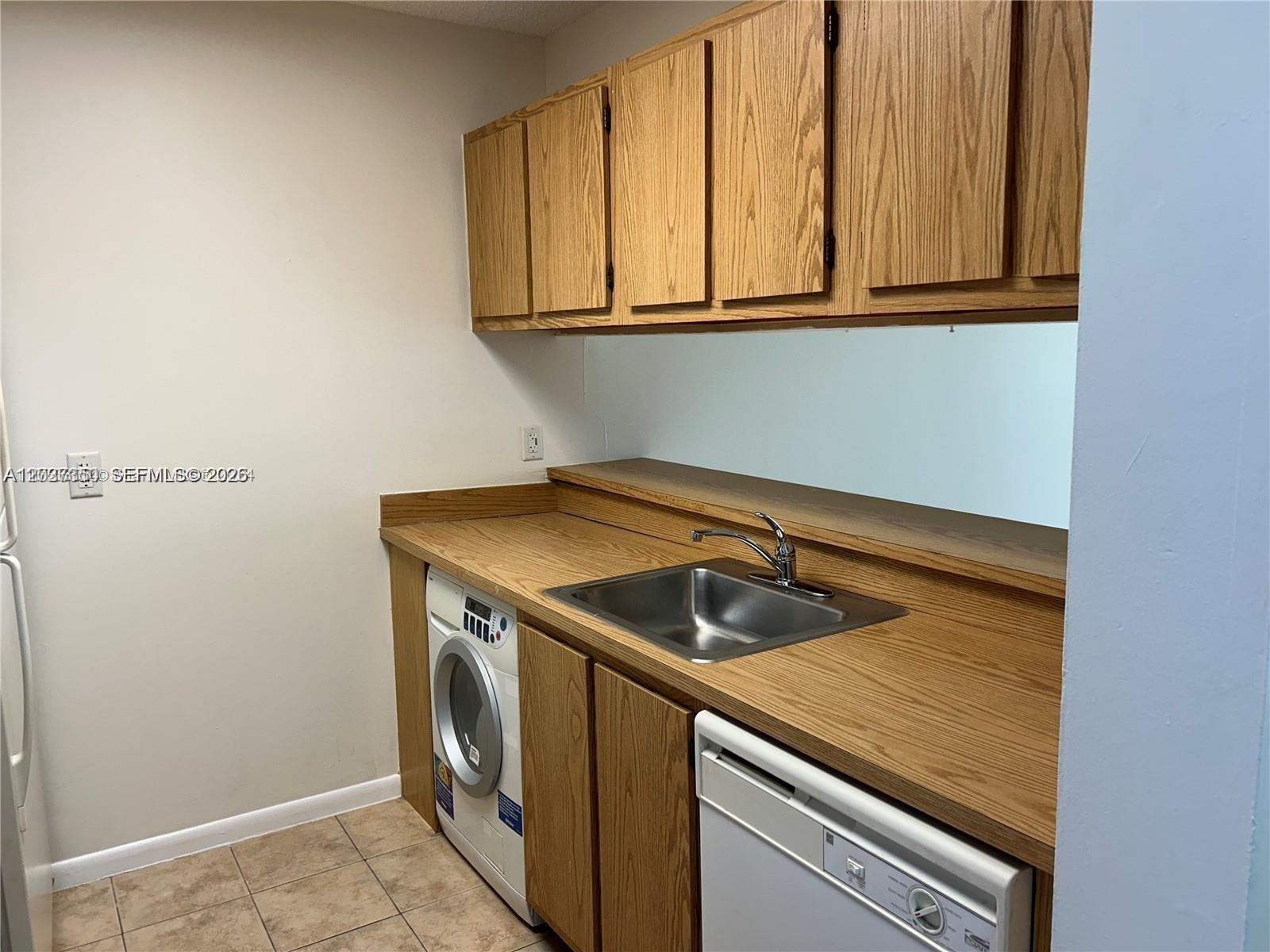 A laundry room features wood cabinets, a laminate countertop, a sink, and a washing machine — 8600 N Sherman Cir # 504, Miramar FL 33025, MIRAMAR, FL