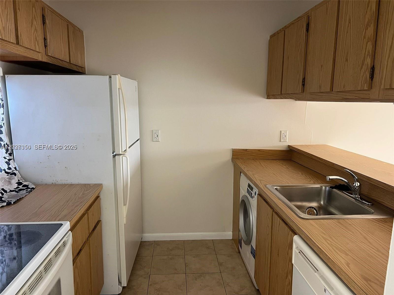 A kitchen features wood cabinets, a white refrigerator, a stainless steel sink, and a washer — 8600 N Sherman Cir # 504, Miramar FL 33025, MIRAMAR, FL