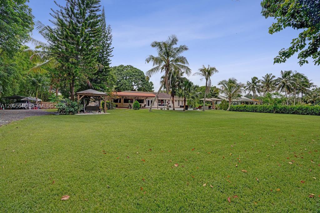 A large grassy backyard features a house, palm trees, and a wooden gazebo — 4981 SW 186th Ave, Southwest Ranches FL 33332, SOUTHWEST RANCHES, FL