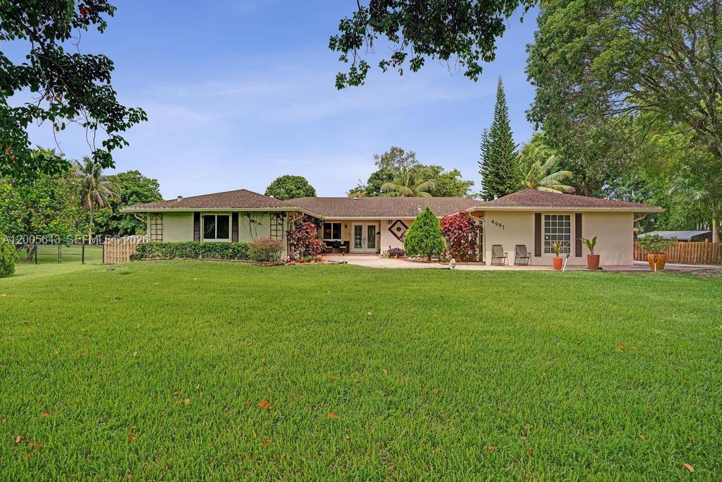 A single-story house with a beige exterior, a large lawn, and a paved patio area — 4981 SW 186th Ave, Southwest Ranches FL 33332, SOUTHWEST RANCHES, FL