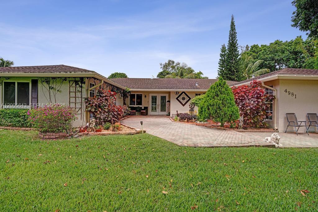 A single-story house with a paved driveway, green lawn, and landscaping under a blue sky — 4981 SW 186th Ave, Southwest Ranches FL 33332, SOUTHWEST RANCHES, FL