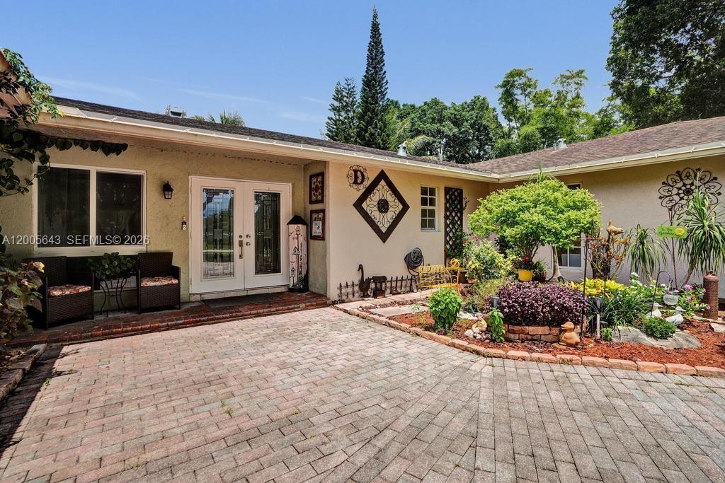 The exterior of a house features a brick patio, double glass doors, and garden landscaping — 4981 SW 186th Ave, Southwest Ranches FL 33332, SOUTHWEST RANCHES, FL