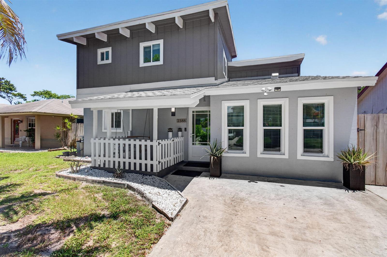 A two-story house features a gray exterior, a white picket fence, and a concrete driveway — 2388 Zeder Avenue, Delray Beach FL 33444, DELRAY BEACH, FL