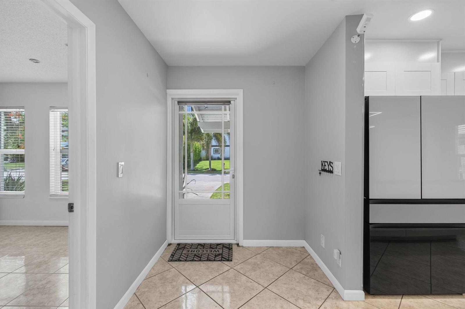 An entryway features light gray walls, tile flooring, a glass-paneled door, and a refrigerator — 2388 Zeder Avenue, Delray Beach FL 33444, DELRAY BEACH, FL