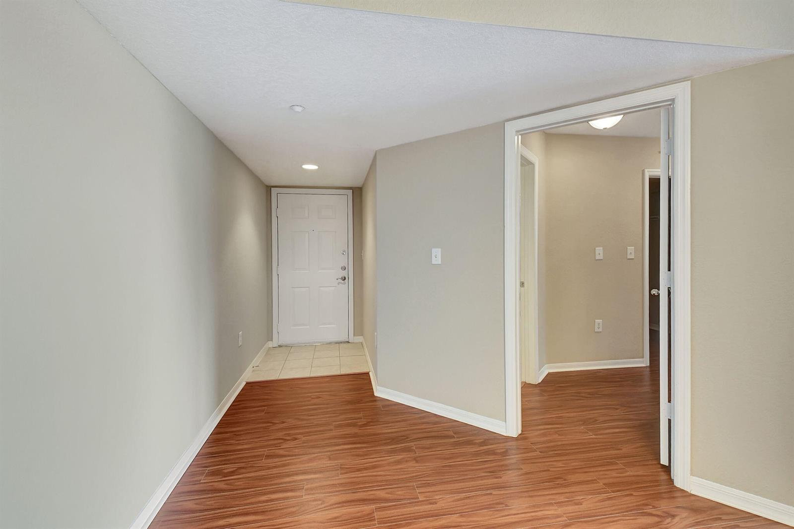 An entryway with wood-look flooring leads to a white front door and an interior hallway — 15065 Michelangelo Boulevard # 305, Delray Beach FL 33446, DELRAY BEACH, FL