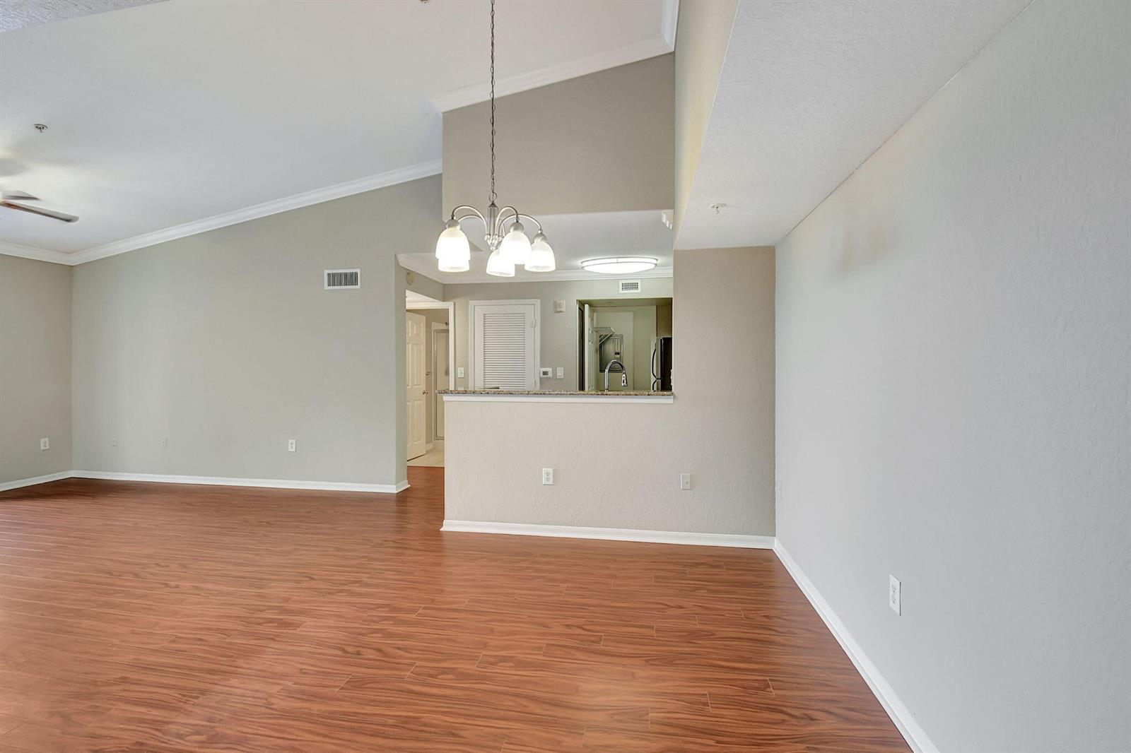 An open living area features vaulted ceilings, wood-look flooring, and a kitchen pass-through window — 15065 Michelangelo Boulevard # 305, Delray Beach FL 33446, DELRAY BEACH, FL