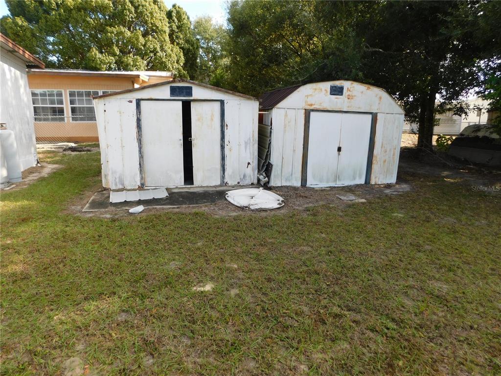 Two weathered metal storage sheds stand on a grassy lot behind a house — 34912 HAWKIOWA ROAD, DADE CITY, FL