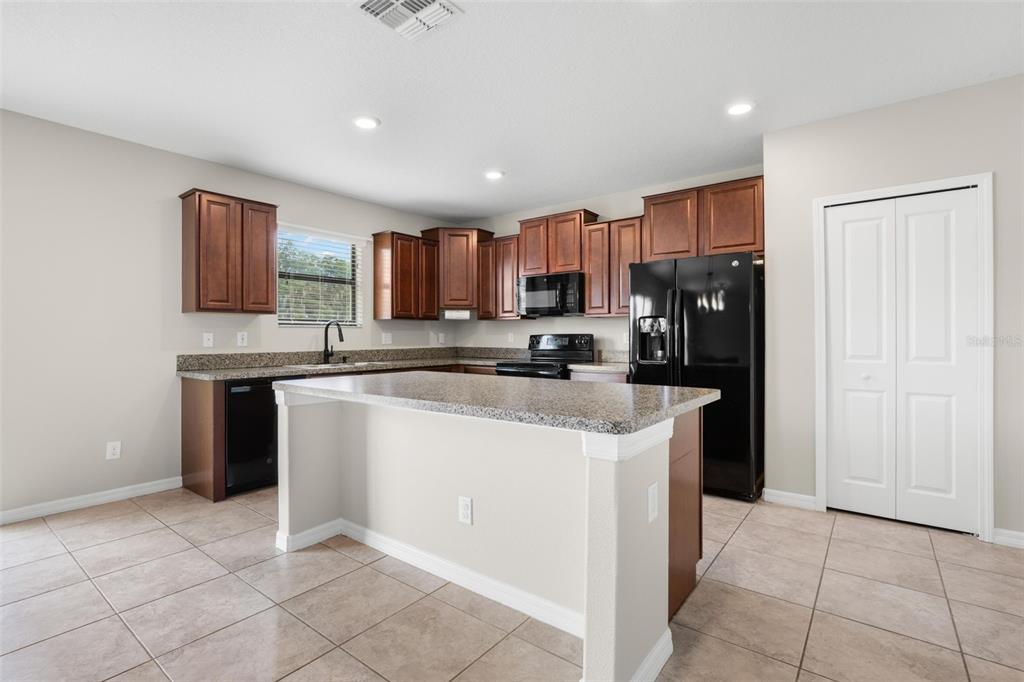 A kitchen features brown cabinets, granite countertops, an island, and black appliances on tile flooring — 36101 STABLE WILK AVENUE, ZEPHYRHILLS, FL