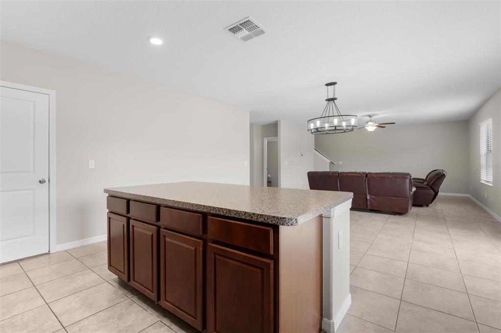 A kitchen island with dark wood cabinets and a speckled countertop faces a living area — 36101 STABLE WILK AVENUE, ZEPHYRHILLS, FL