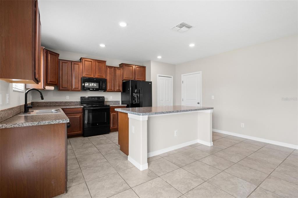 A kitchen features dark wood cabinets, black appliances, granite countertops, and a central island — 36101 STABLE WILK AVENUE, ZEPHYRHILLS, FL