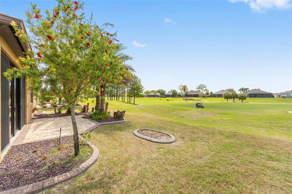 A backyard patio with a small tree overlooks a grassy golf course under a blue sky — 6816 SW 95TH CIRCLE, OCALA, FL