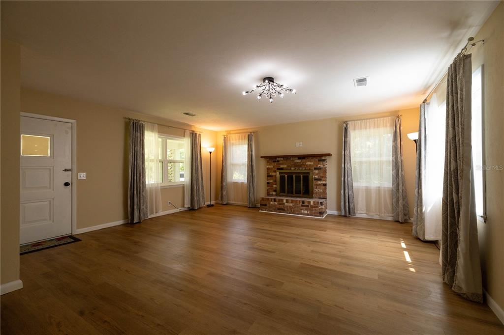 A living room features wood-look flooring, a brick fireplace, and a modern light fixture — 298 N COURT STREET, BRONSON, FL