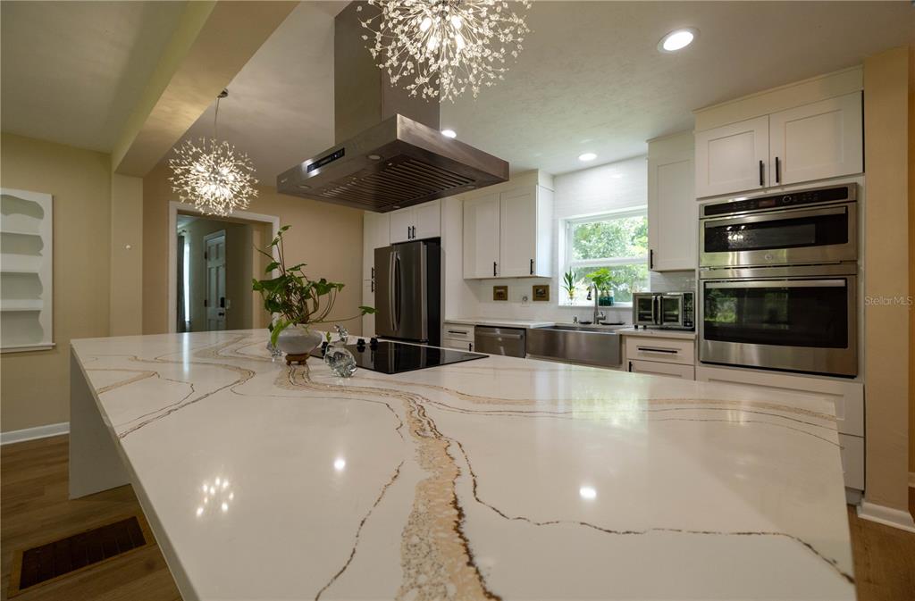 A modern kitchen features a large white quartz island, stainless steel appliances, and pendant lighting — 298 N COURT STREET, BRONSON, FL