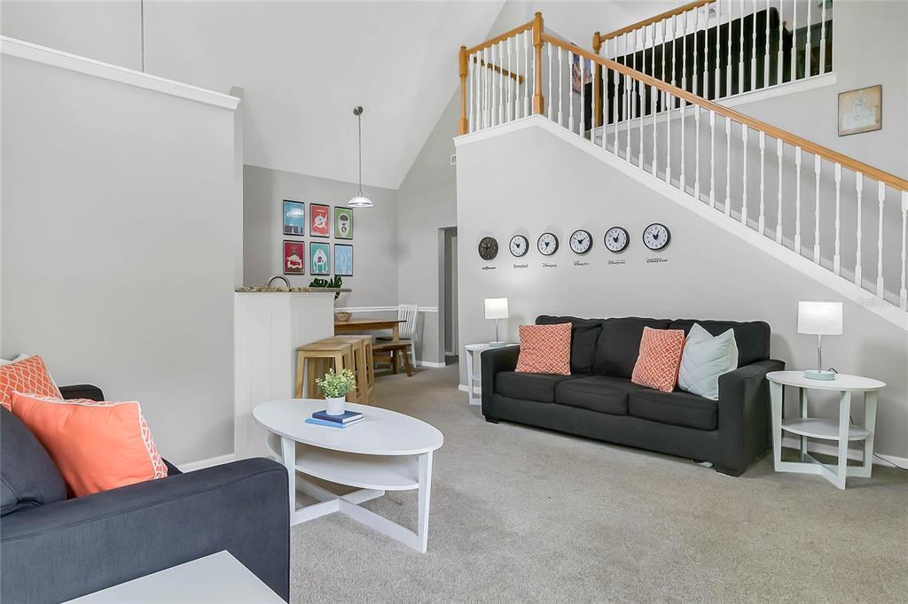 A living room features a dark sofa, a white coffee table, and a staircase with wooden railings — 3017 BONFIRE BEACH DRIVE UNIT 203, KISSIMMEE, FL