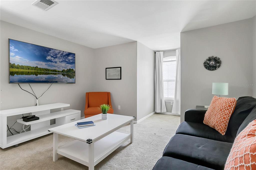 A living room features a television, white media console, coffee table, orange armchair, and dark sofa — 3017 BONFIRE BEACH DRIVE UNIT 203, KISSIMMEE, FL