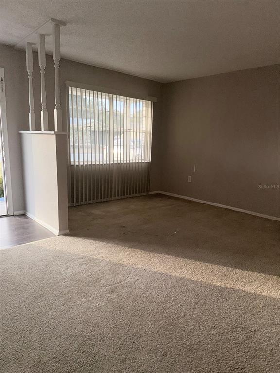 A living room features beige carpeting, a half-wall with white spindles, and vertical window blinds — 878 KILLEARN BOULEVARD, WINTER HAVEN, FL