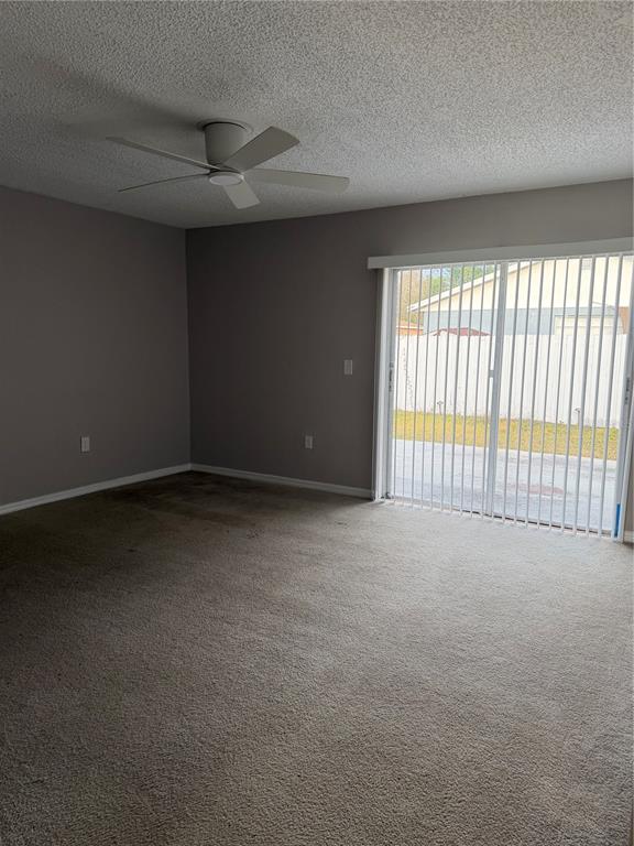 An empty room features gray walls, beige carpeting, a ceiling fan, and sliding glass doors — 878 KILLEARN BOULEVARD, WINTER HAVEN, FL