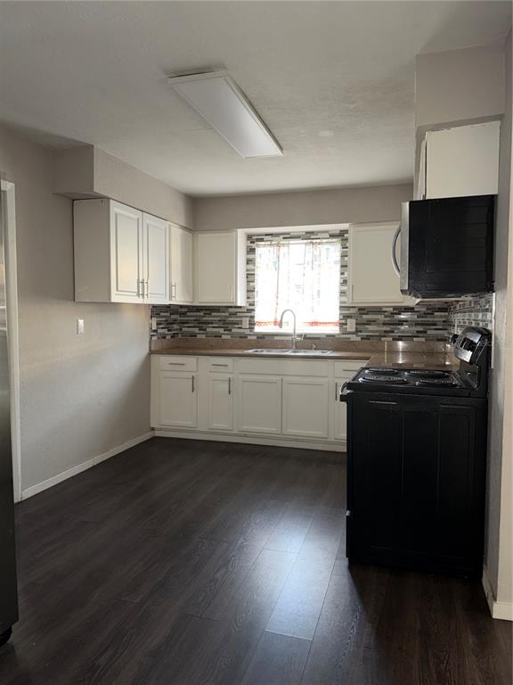 A kitchen features white cabinets, dark wood-look flooring, a black stove, and a tiled backsplash — 878 KILLEARN BOULEVARD, WINTER HAVEN, FL
