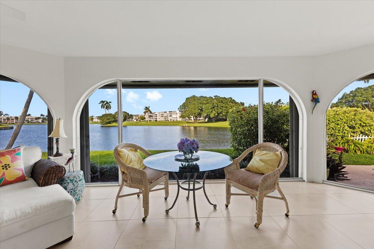 A sunroom with tile floors features a glass dining table overlooking a lake and greenery — 233 Rio Vista Circle # 233, Atlantis FL 33462, ATLANTIS, FL