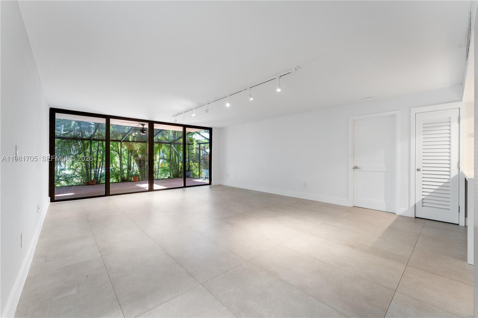 A bright, empty room with large glass sliding doors, track lighting, and light-colored tile flooring — 55 Ocean Lane Dr # 1031, Key Biscayne FL 33149, KEY BISCAYNE, FL