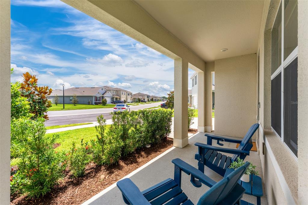 A covered porch features two blue Adirondack chairs overlooking a suburban street and neighborhood homes — 3366 EASTGROVE TERRACE, SANFORD, FL