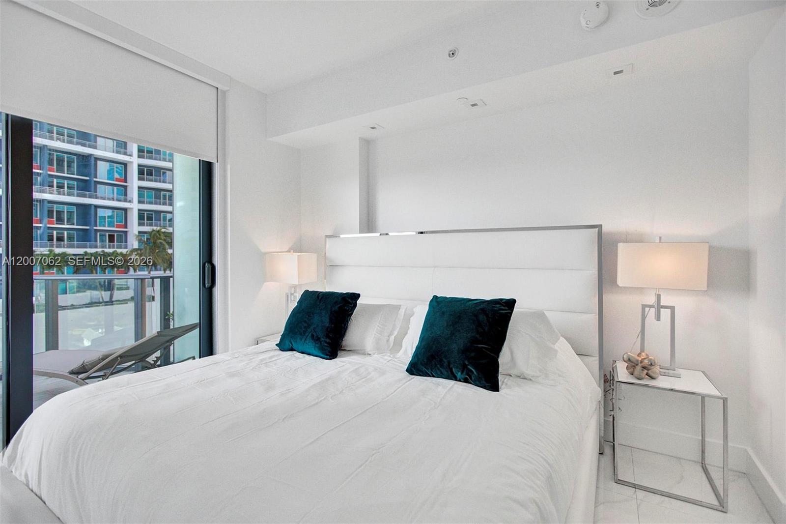 A modern bedroom features a white upholstered headboard, teal accent pillows, and a private balcony — 1300 S Miami Ave # 1407, Miami FL 33130, MIAMI, FL