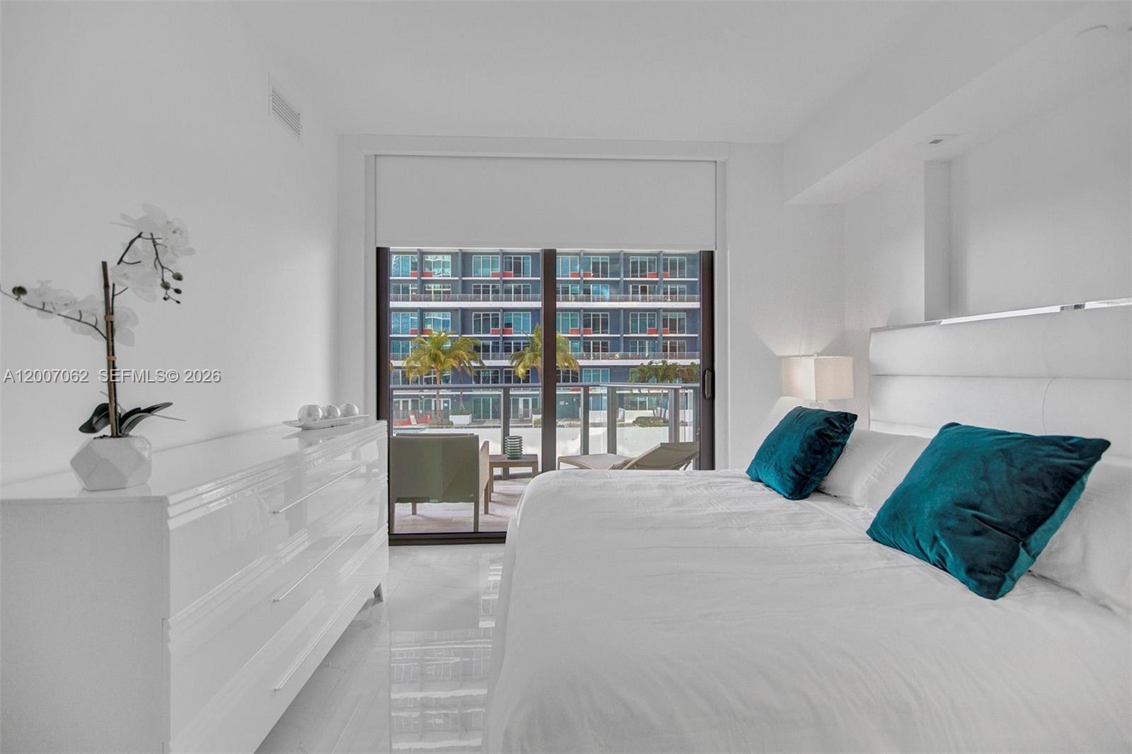 A modern bedroom features a white dresser, a bed with teal pillows, and a balcony — 1300 S Miami Ave # 1407, Miami FL 33130, MIAMI, FL