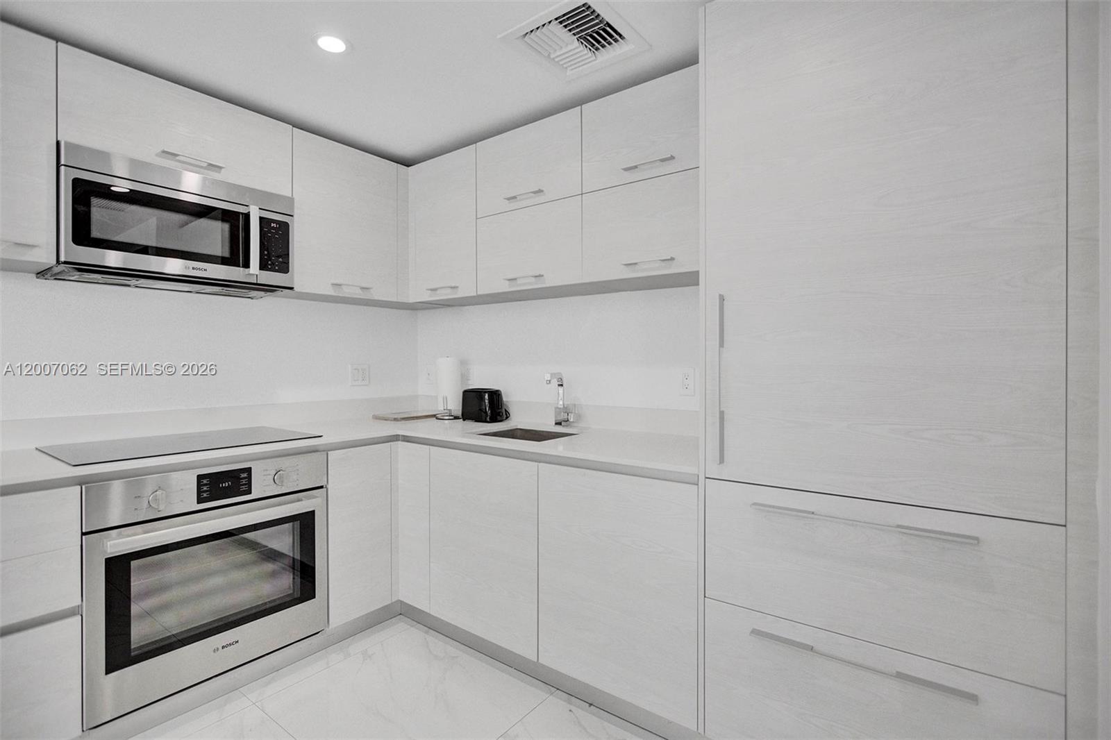 A modern kitchen features white wood-grain cabinets, stainless steel appliances, and white marble-style flooring — 1300 S Miami Ave # 1407, Miami FL 33130, MIAMI, FL