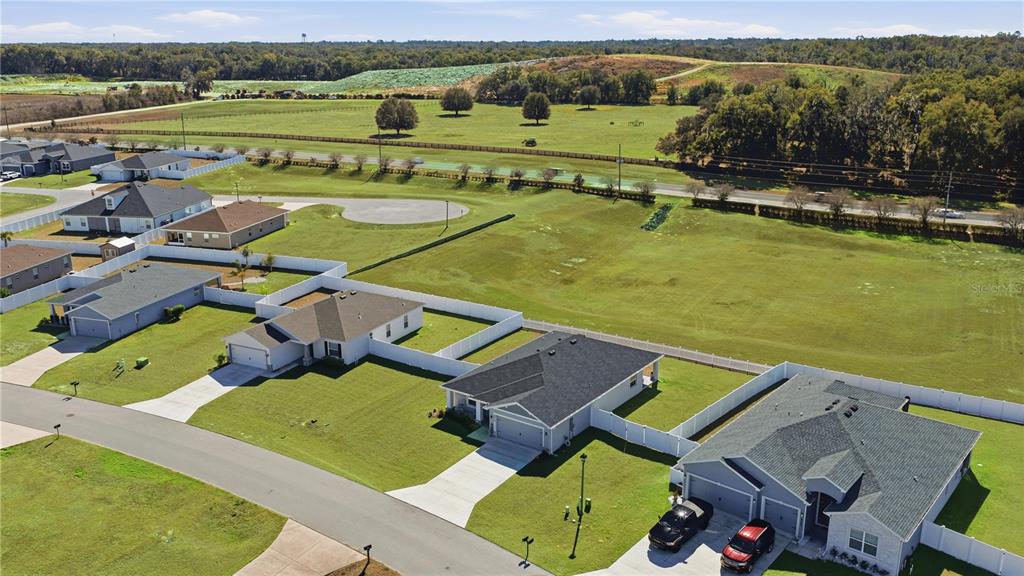 An aerial view shows several suburban houses with white vinyl fences bordering a large field — 4810 SE 91ST PLACE, OCALA, FL