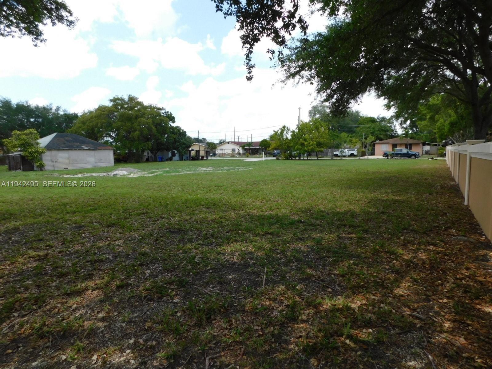 A large, flat, grassy vacant lot is bordered by trees and a tan wall — 5830 Liberty St, Hollywood FL 33021, HOLLYWOOD, FL