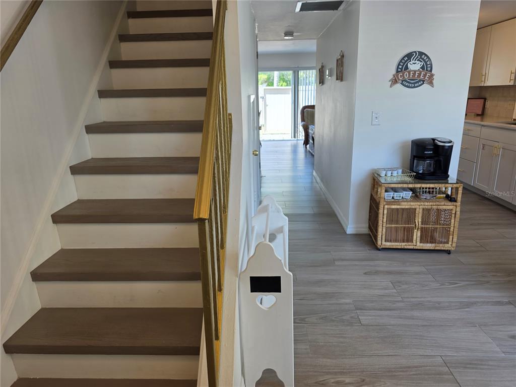 A staircase with wooden treads and a gold railing sits beside a hallway and kitchen — 4215 E BAY DRIVE UNIT 1403, CLEARWATER, FL