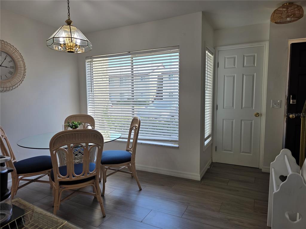 A dining area features a glass-topped table, rattan chairs, wood-look flooring, and a white door — 4215 E BAY DRIVE UNIT 1403, CLEARWATER, FL