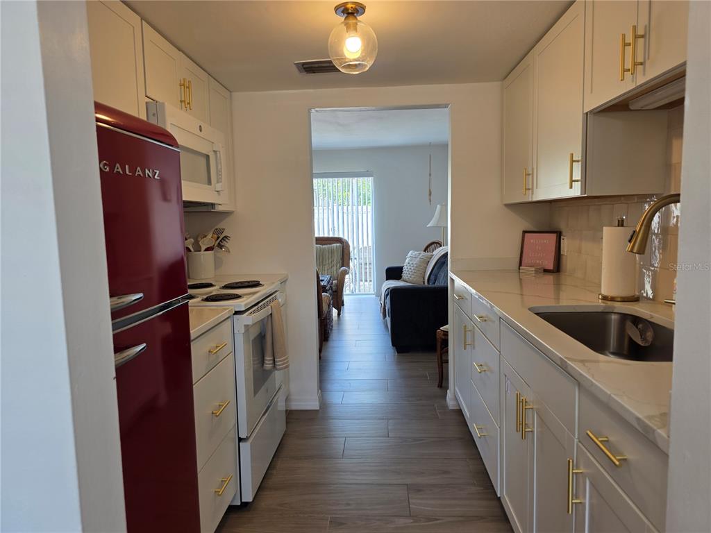 A galley kitchen features white cabinets, gold hardware, a red refrigerator, and wood-look tile flooring — 4215 E BAY DRIVE UNIT 1403, CLEARWATER, FL