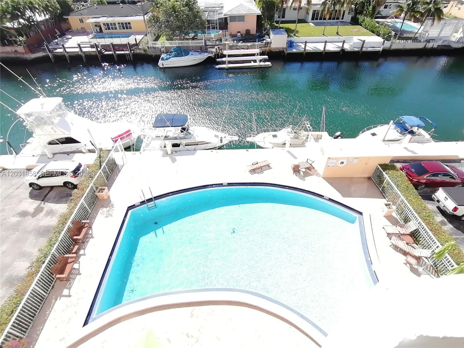 An elevated view shows a swimming pool, parked cars, and boats docked in a canal — 2020 NE 135th St # 506, North Miami FL 33181, NORTH MIAMI, FL