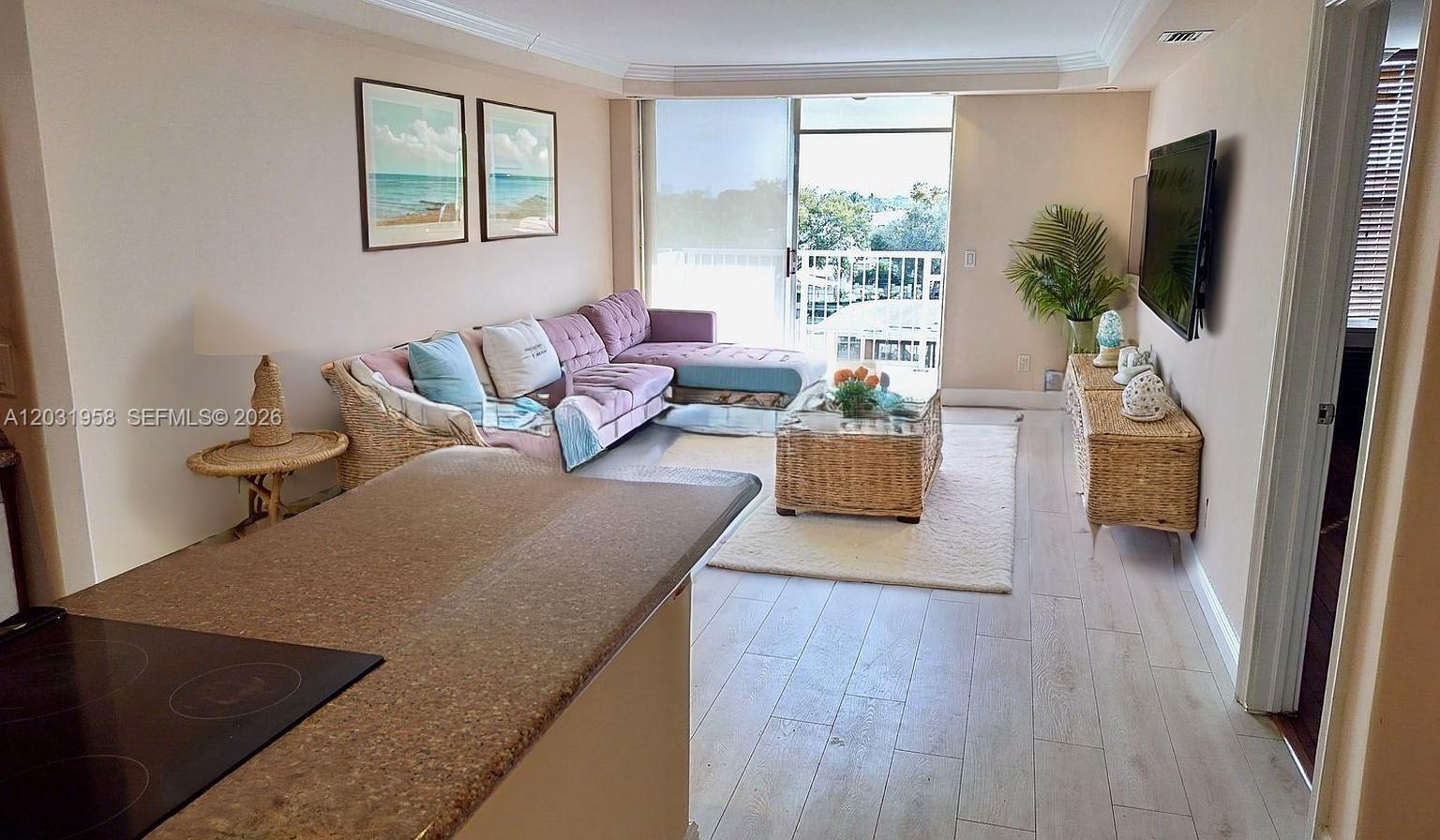 A living room features a purple sectional sofa, wicker furniture, and a balcony view — 2020 NE 135th St # 506, North Miami FL 33181, NORTH MIAMI, FL