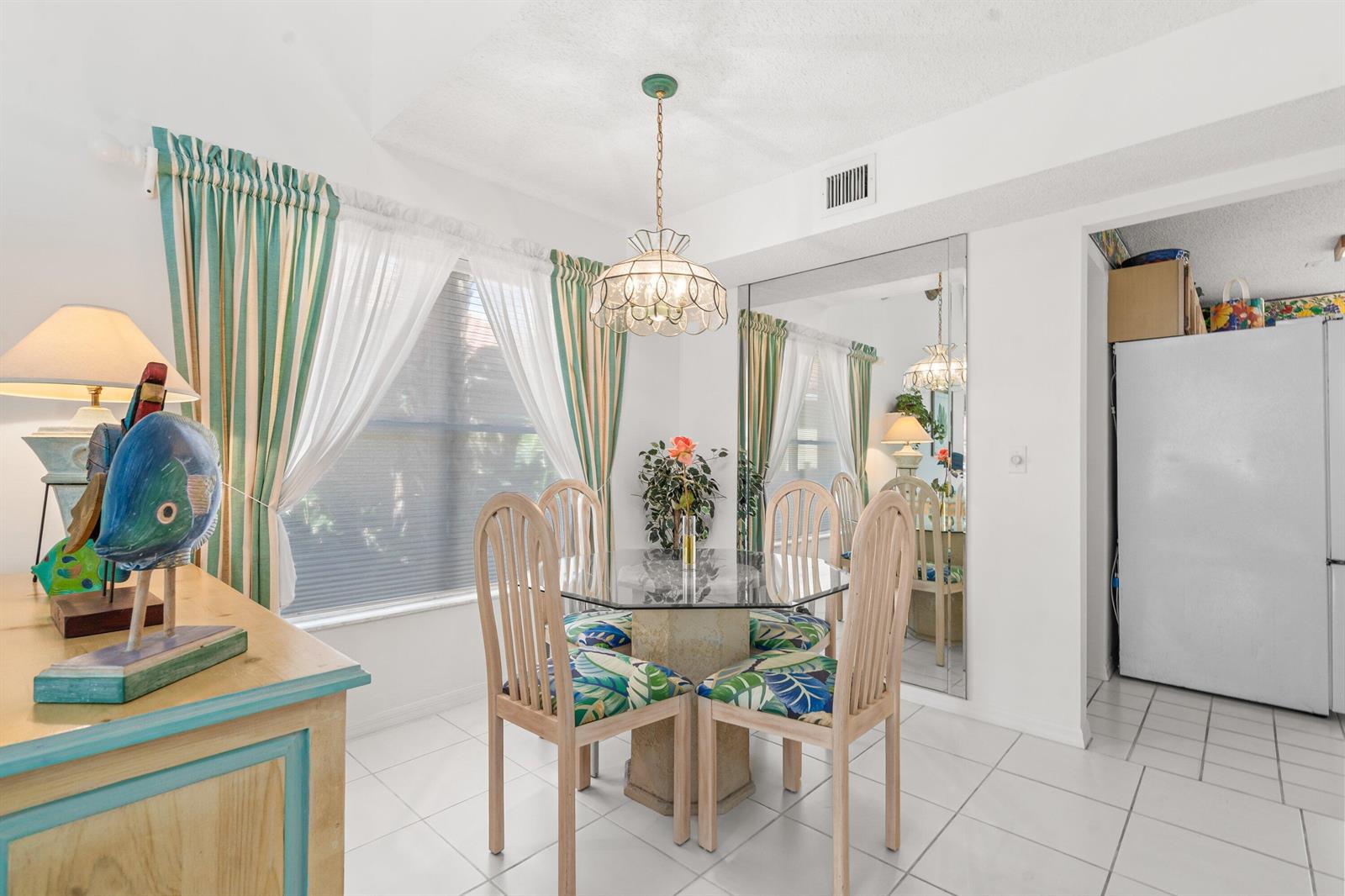 A dining area features a glass-topped table, four chairs, a chandelier, and a large mirror — 2746 Linkside Drive, Wellington FL 33414, WELLINGTON, FL