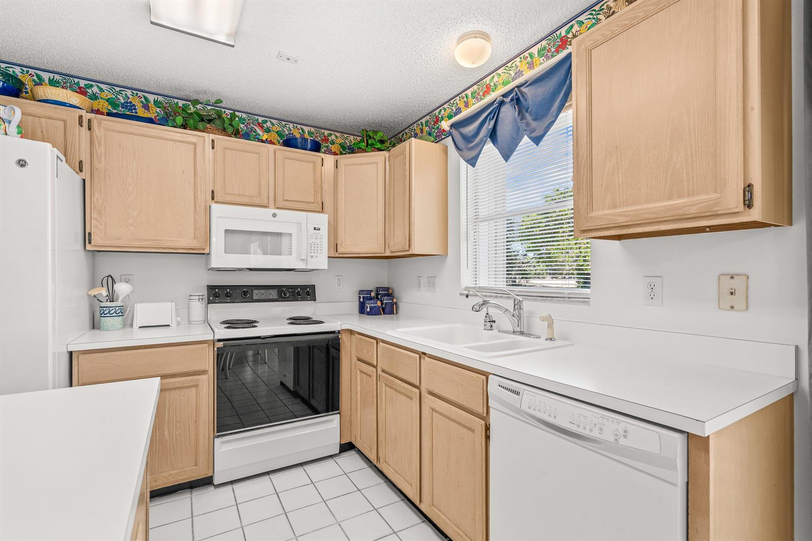 A kitchen features light wood cabinets, white appliances, white countertops, and a tiled floor — 2746 Linkside Drive, Wellington FL 33414, WELLINGTON, FL