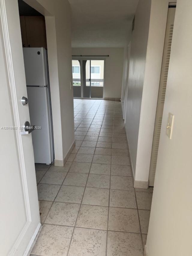 A tiled hallway leads from an entryway past a white refrigerator toward a glass door — 7740 Camino Real # 306, Miami FL 33143, MIAMI, FL