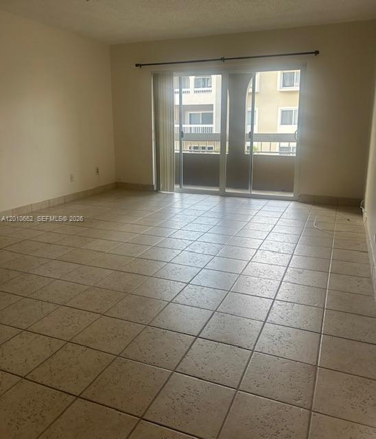 An empty room with beige tile flooring and a sliding glass door leading to a balcony — 7740 Camino Real # 306, Miami FL 33143, MIAMI, FL