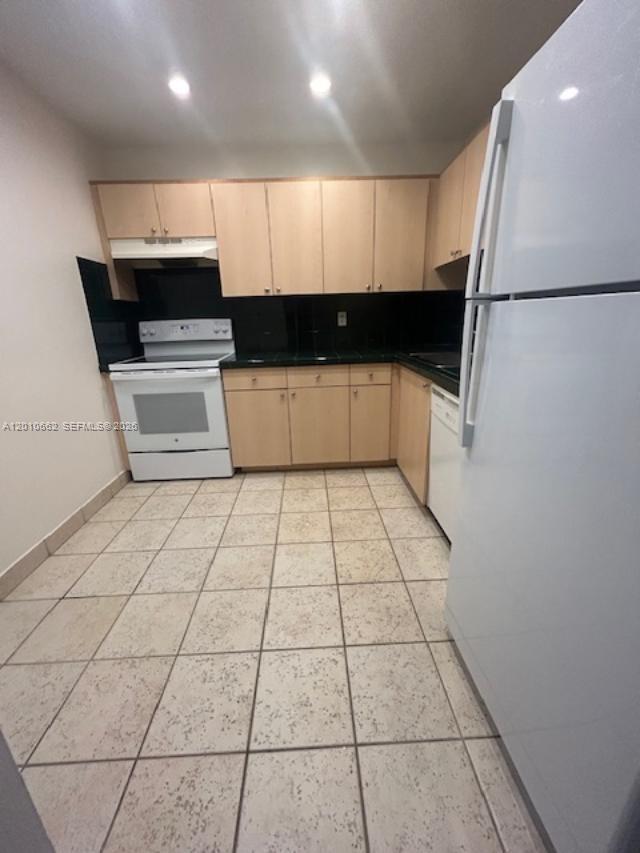 A kitchen features light wood cabinets, a white stove, a white refrigerator, and tiled floors — 7740 Camino Real # 306, Miami FL 33143, MIAMI, FL