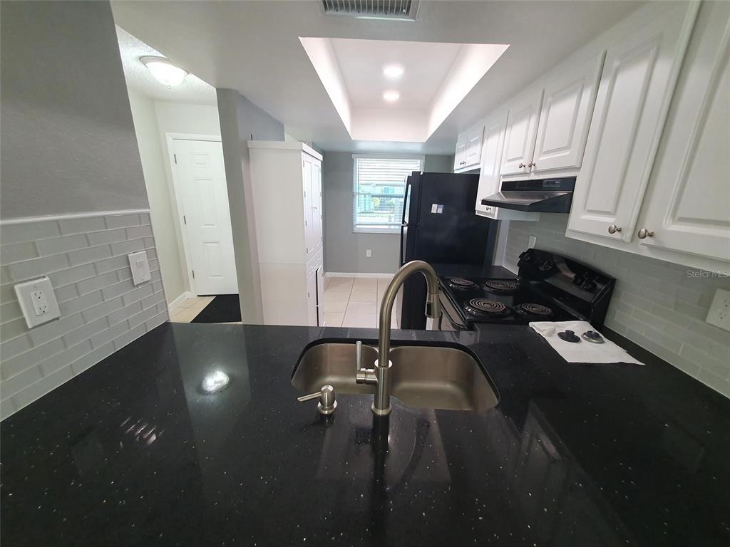 A kitchen features black countertops, white cabinets, stainless steel sink, and black appliances — 1893 ORANGE BOULEVARD WAY, PALM HARBOR, FL