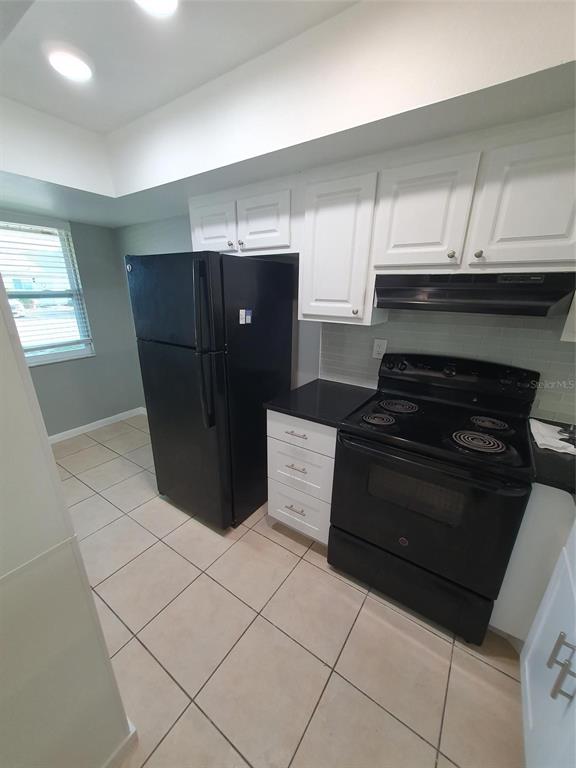 A kitchen features white cabinets, black appliances, black countertops, and light-colored tile flooring — 1893 ORANGE BOULEVARD WAY, PALM HARBOR, FL