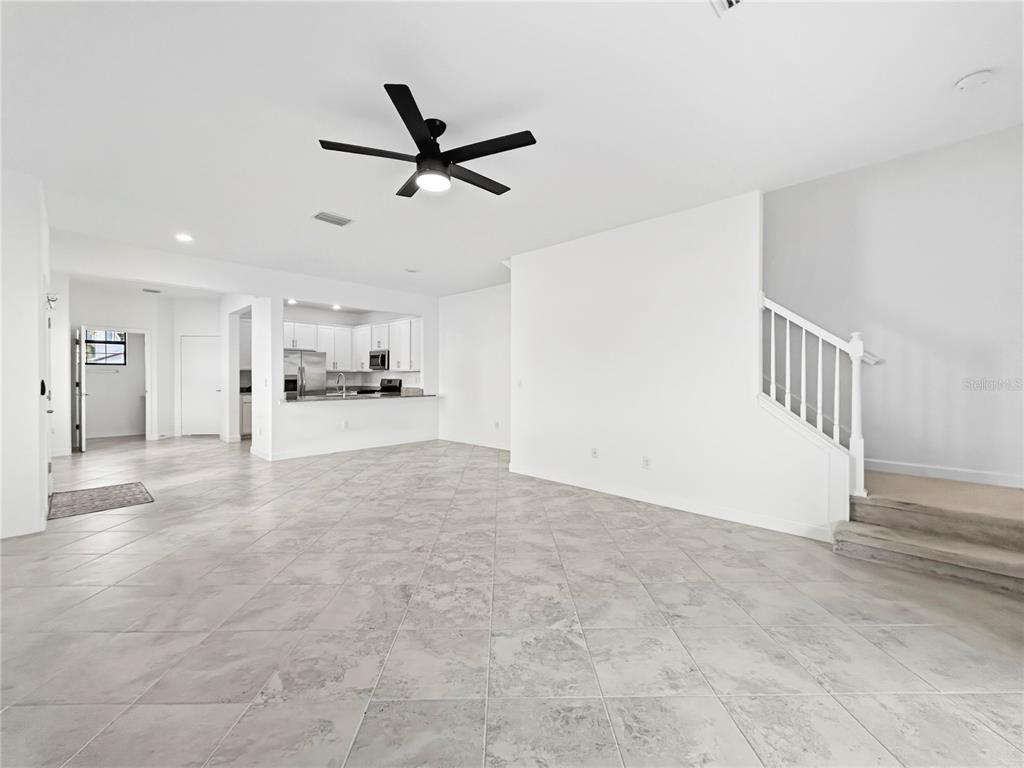 An open-concept living area features light tile flooring, a ceiling fan, and a staircase — 15148 LYLA TERRACE, BRADENTON, FL