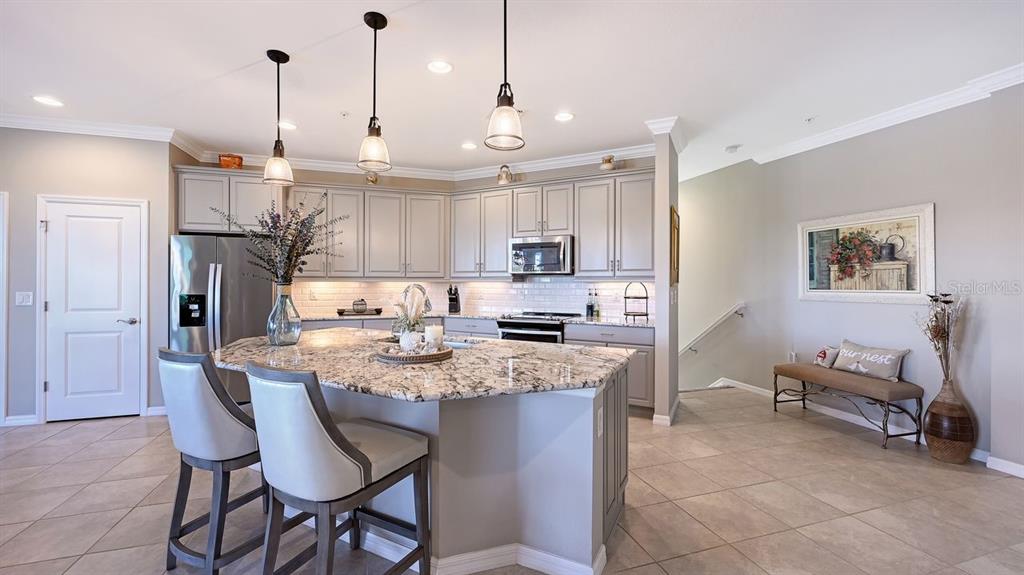 A kitchen features a granite-topped island, gray cabinetry, stainless steel appliances, and tile flooring — 23149 BANBURY WAY UNIT 201, VENICE, FL