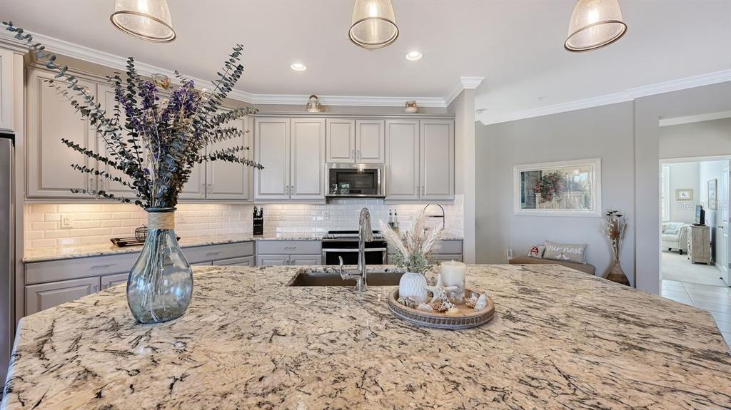 A kitchen features light gray cabinets, granite countertops, a large island, and white subway tile backsplash — 23149 BANBURY WAY UNIT 201, VENICE, FL