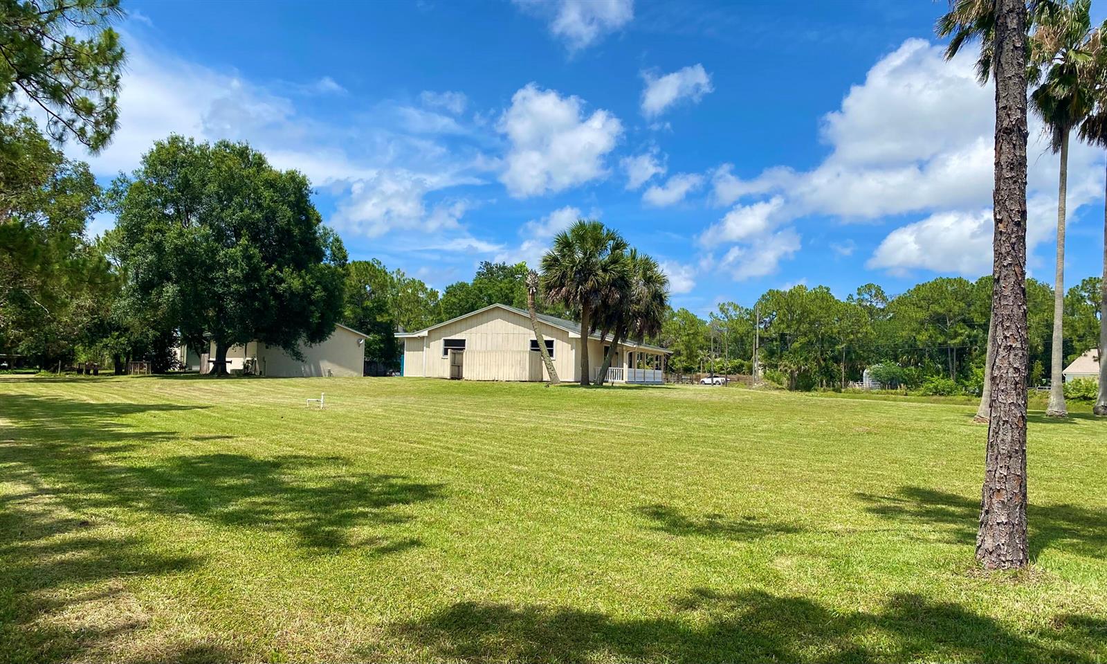 A light-colored house sits on a large, grassy lot surrounded by trees under a blue sky — 10531 151st Lane N, Jupiter FL 33478, JUPITER, FL