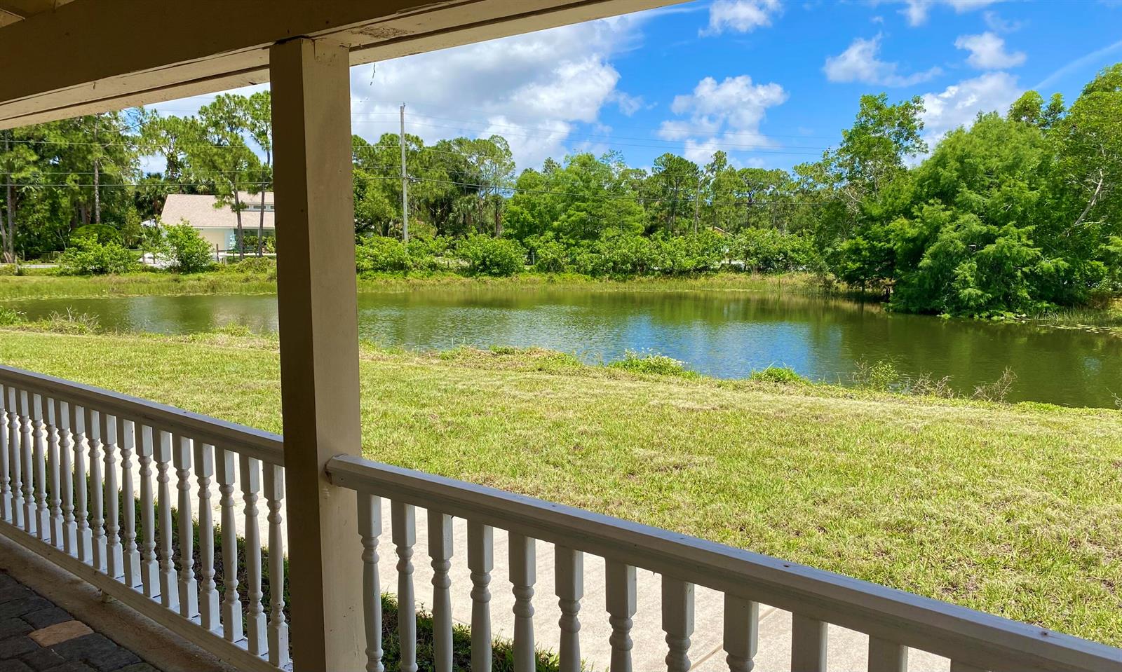 A view of a grassy yard and pond from a covered porch with white railings — 10531 151st Lane N, Jupiter FL 33478, JUPITER, FL
