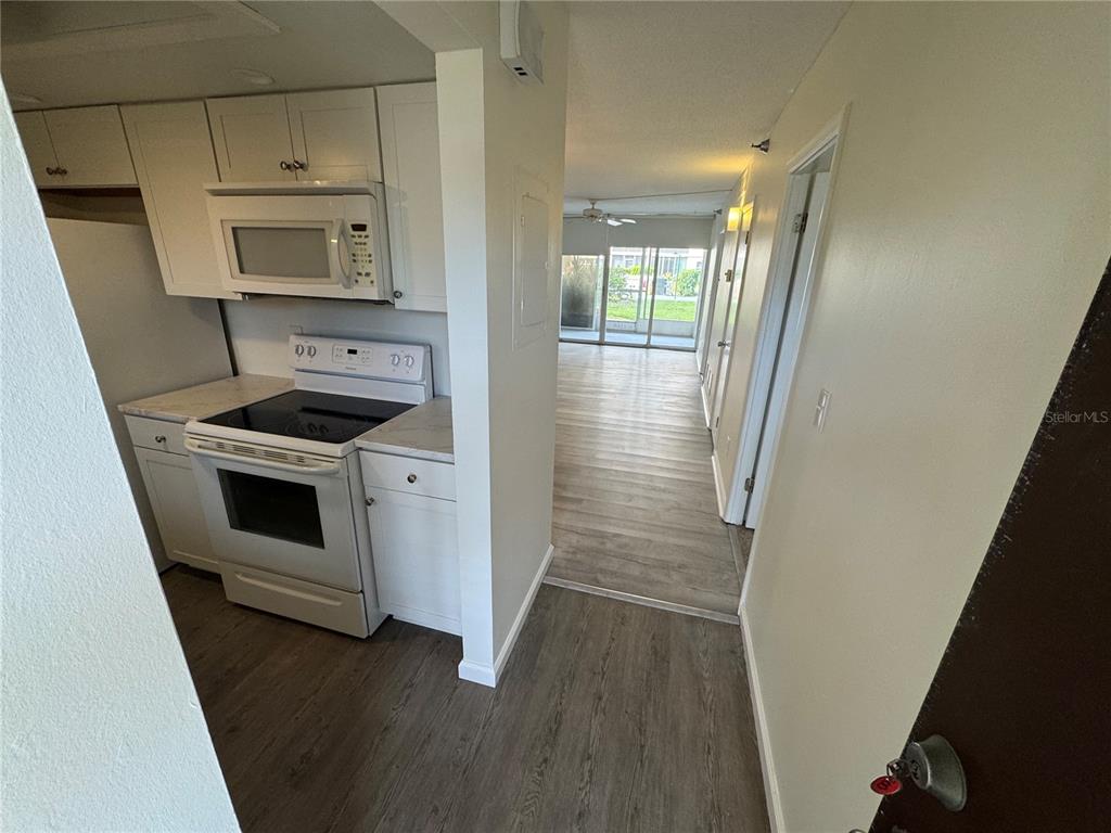 A kitchen with white cabinets and appliances opens into a living area with sliding doors — 232 SAINT AUGUSTINE AVENUE UNIT 102, VENICE, FL