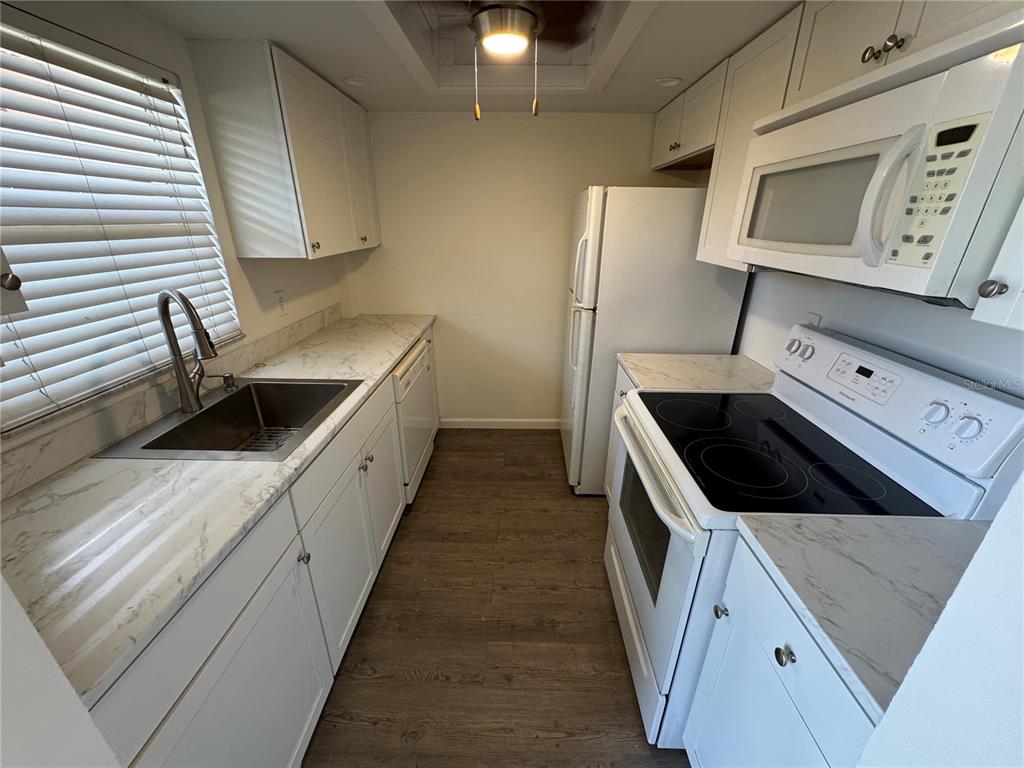 A galley kitchen features white cabinets, marble-look countertops, stainless steel appliances, and wood-look flooring — 232 SAINT AUGUSTINE AVENUE UNIT 102, VENICE, FL